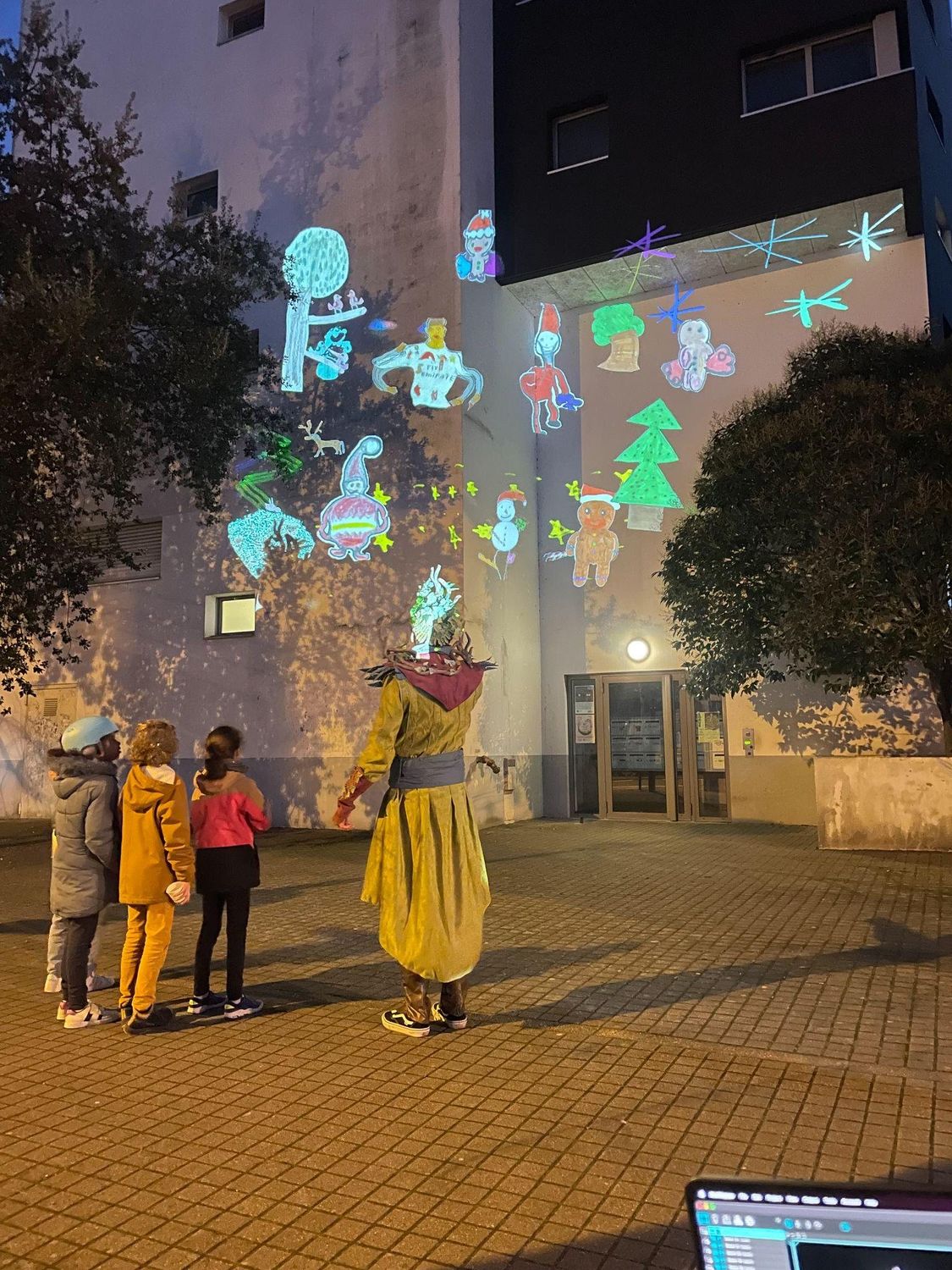 Passants observant une projection de personnages animés sur la façade d’un immeuble, le soir.