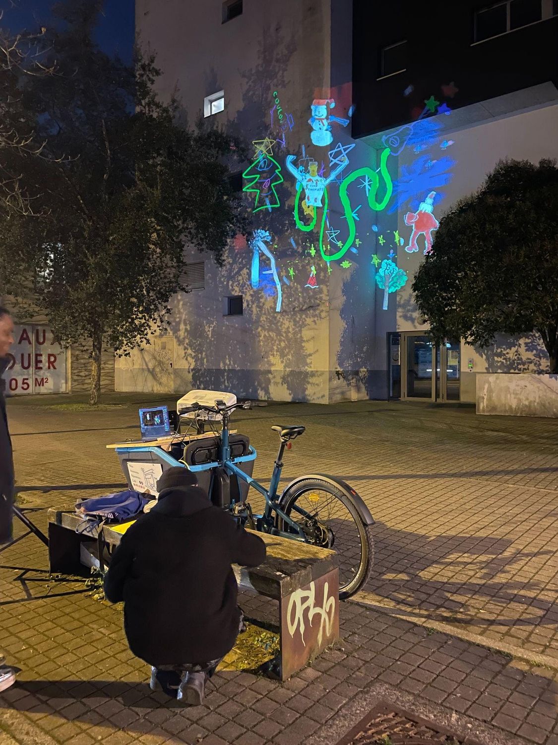 Triporteur équipé d’un vidéoprojecteur autonome, en pleine projection dans la rue.