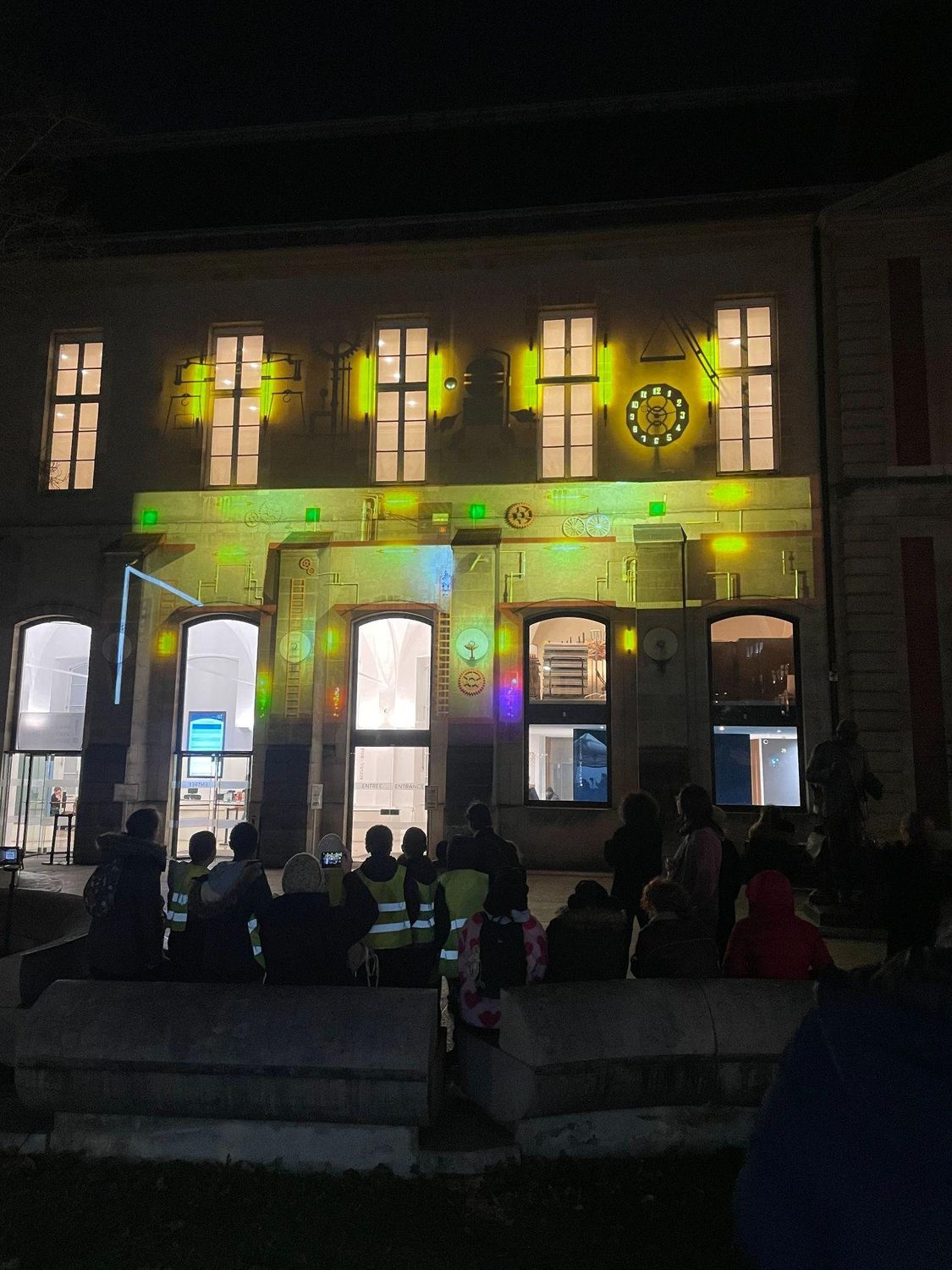 Public rassemblé devant une façade patrimoniale illuminée par une projection mapping.